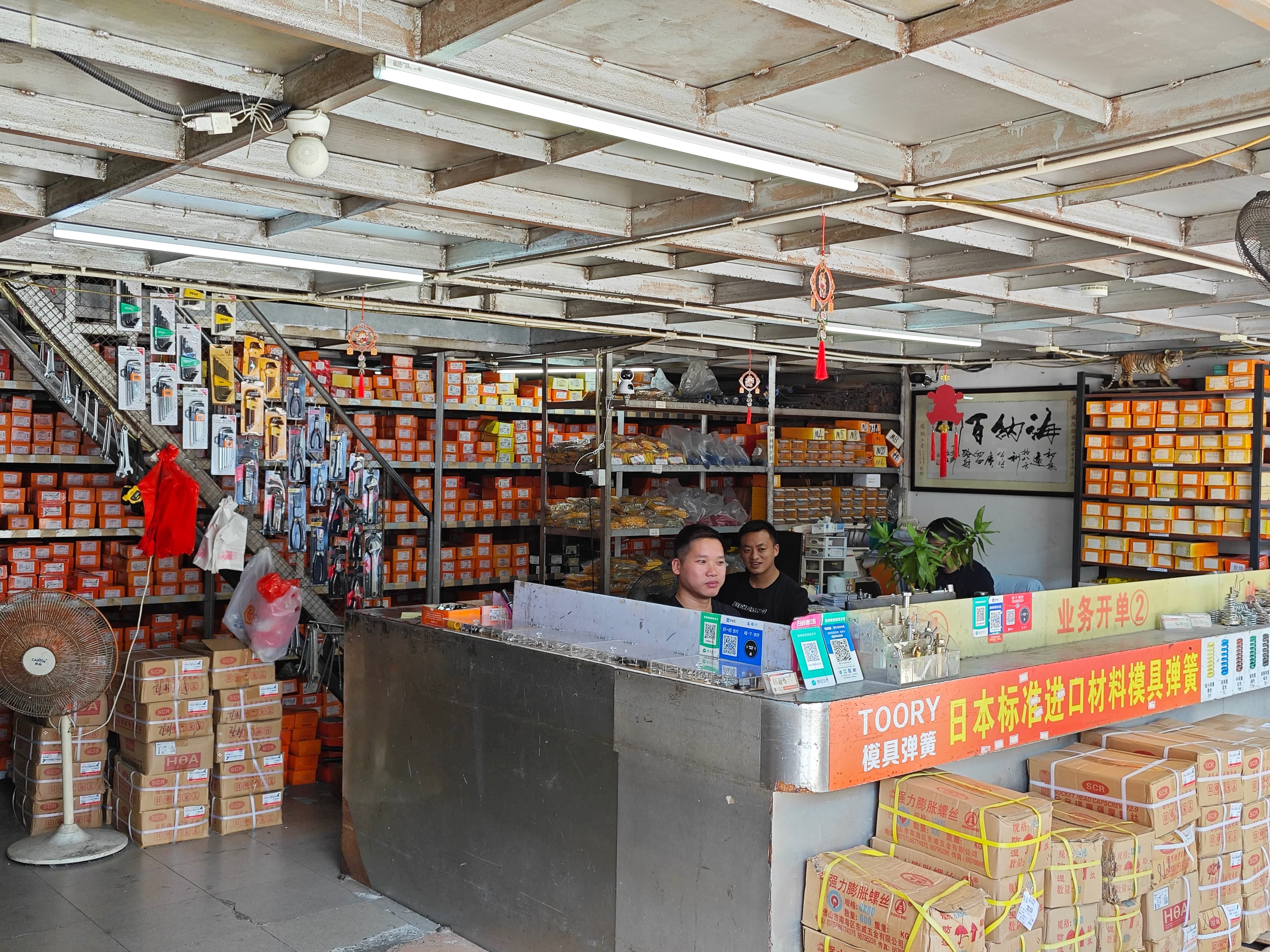 People at the Yulong shop counter with labelled fastener boxes on the shelves behind them.